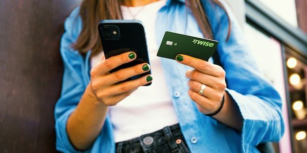 一位穿著藍色襯衫的用戶手中同時拿著智慧型手機與一張深綠色 Wise 商務金融卡,特寫展示卡片設計與行動支付的應用場景。