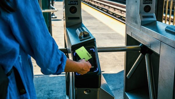 一位旅客在火車站或地鐵站閘門,使用亮綠色的 Wise 卡進行感應式支付過閘,展示其在海外旅遊交通的便利性。